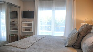 Une chambre à coucher avec un lit, un téléviseur fixé au mur, une fenêtre avec des rideaux et un balcon.