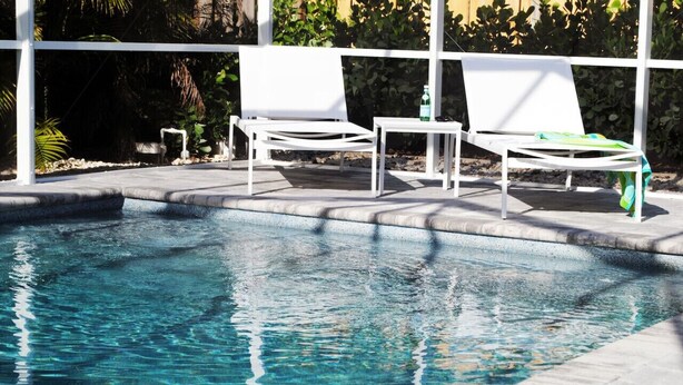 Une piscine aux eaux cristallines, agrémentée de deux chaises longues blanches et d’une petite table.