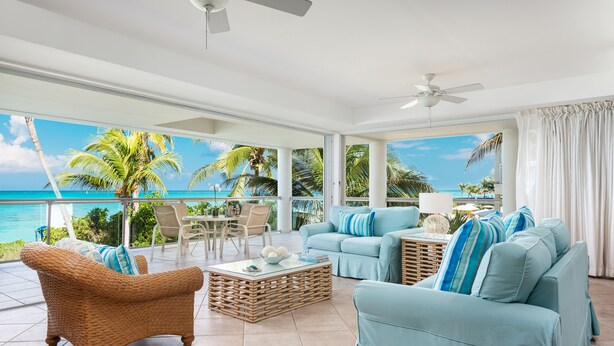A spacious living area with a view of the ocean, featuring wicker furniture, a light blue sofa, and a ceiling fan. - Gorgeous second floor, ocean front with huge wrap around balcony!!! (Providenciales)