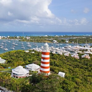 Un phare entouré d’une végétation luxuriante, une marina où sont amarrés de nombreux bateaux et une ville côtière avec ses bâtiments.
