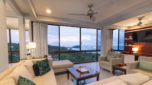 A spacious living room with a large sofa, a coffee table, and a television. The room has large windows offering a view of the sea and greenery. - Villa Tortuga: Ocean Views Chef Included, Daily Housekeeping & Concierge Service (Quepos)