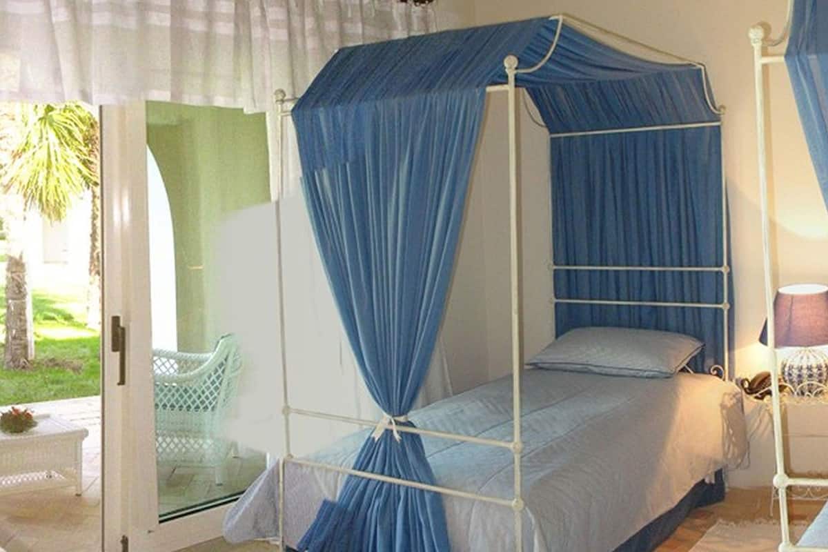 A single bed with a canopy in a room with a glass door leading to a garden.