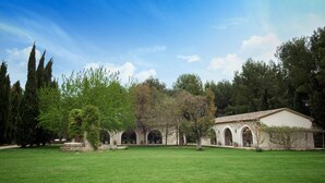 Un patio con un edificio que presenta puertas de arco y un techo de tejas, rodeado de césped verde y árboles.