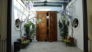 Una habitación amplia con una gran puerta de madera, dos camas con ropa de cama colorida, un altavoz y plantas colgantes.