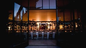 Un espacio de comedor al aire libre con mesas y sillas, rodeado de paredes de vidrio y un interior cálido.