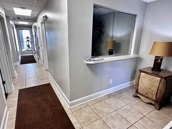 A hallway with a brown rug, a window with a lamp, and a woven cabinet.