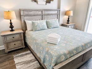 Quarto com cama, duas mesas de cabeceira, cabeceira de madeira, edredom estampado e tapete tecido.