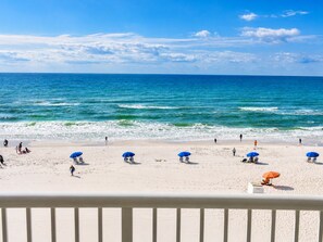 A beach with clear blue water, people walking, and beach umbrellas.