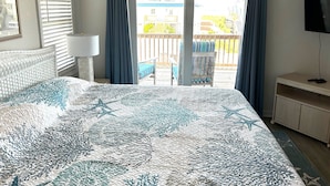 A bedroom with a large bed, a TV, and a balcony with a chair and table.