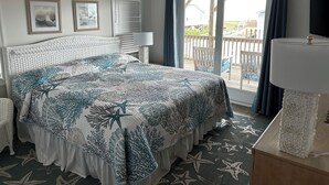 A bedroom with a bed, a ceiling fan, a window with curtains, a view of the outside, and a TV on a stand.