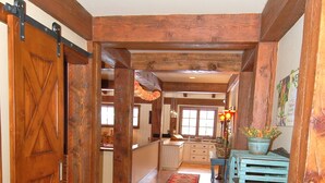 Un couloir en bois avec un tapis à motifs, un banc bleu et une porte dotée d’un loquet métallique.