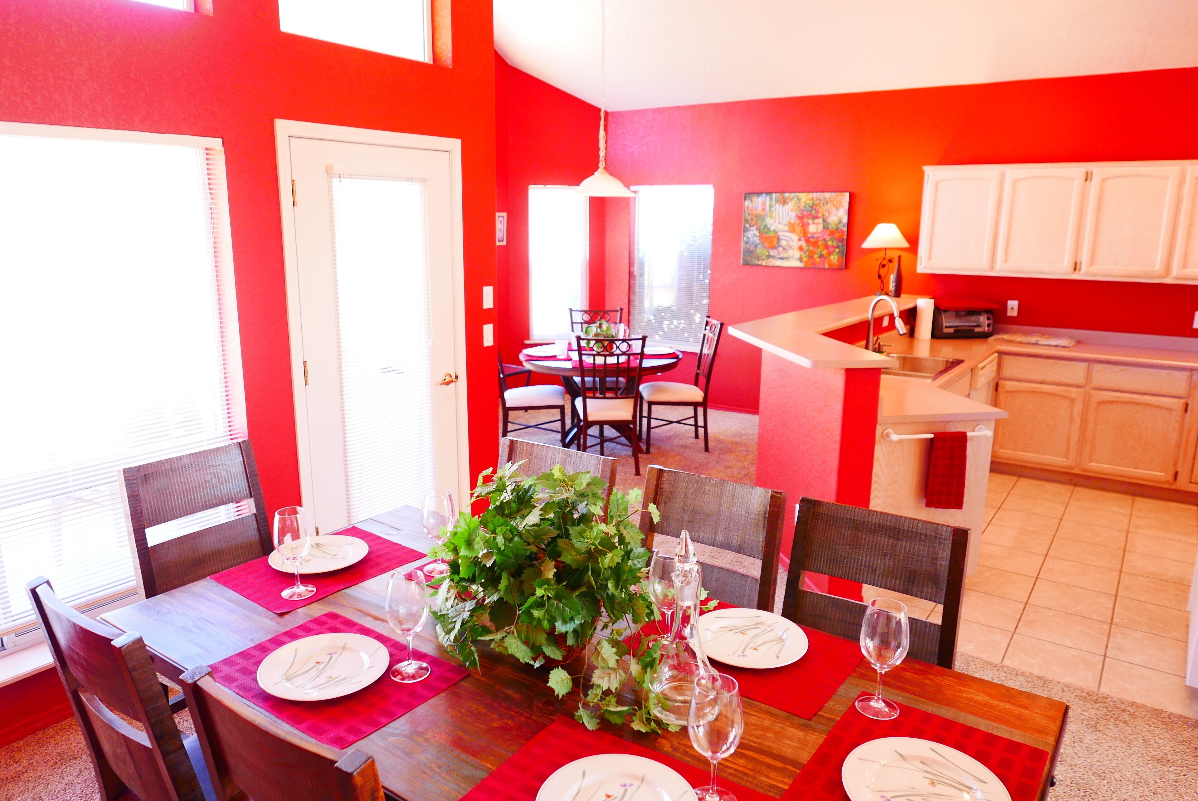 Un coin repas avec une table rouge, des chaises blanches et une grande plante servant de centre de table.