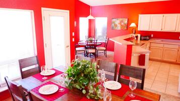 Un coin repas avec une table rouge, des chaises blanches et une grande plante servant de centre de table.