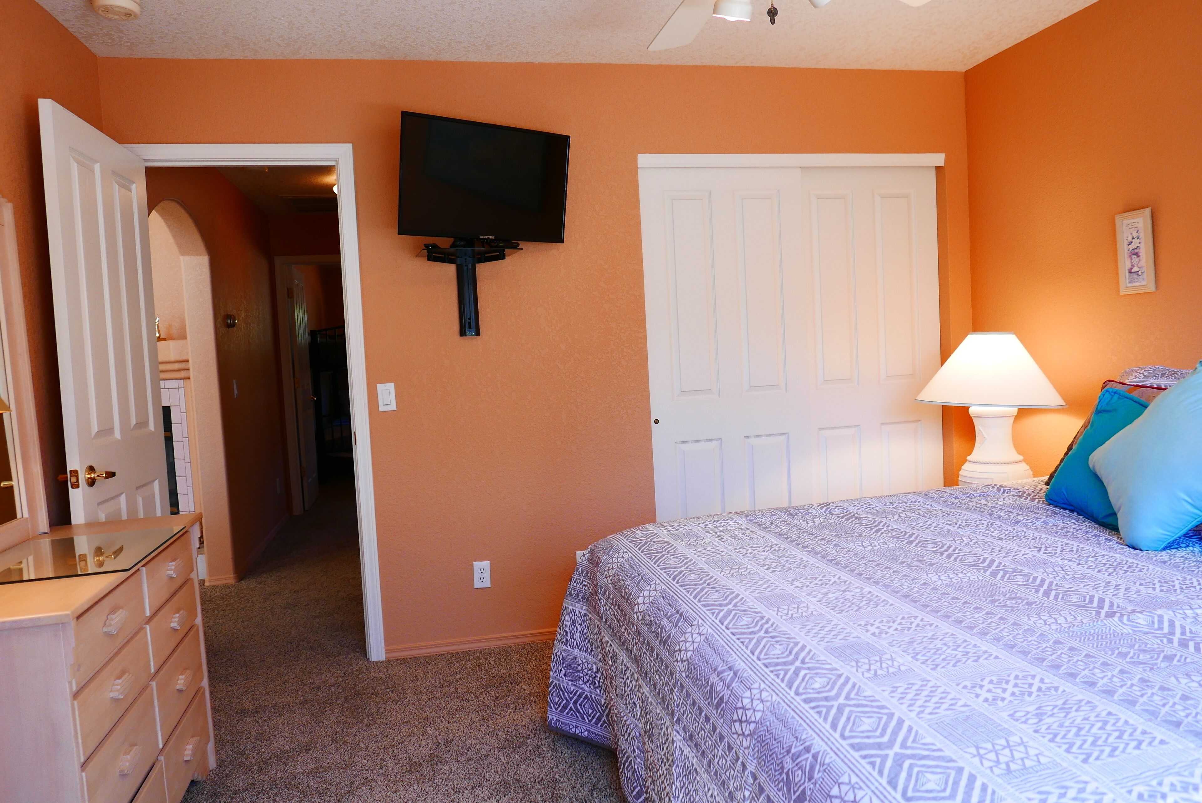 Une chambre à coucher comprenant un lit, une commode, un téléviseur et une porte donnant sur une autre pièce.