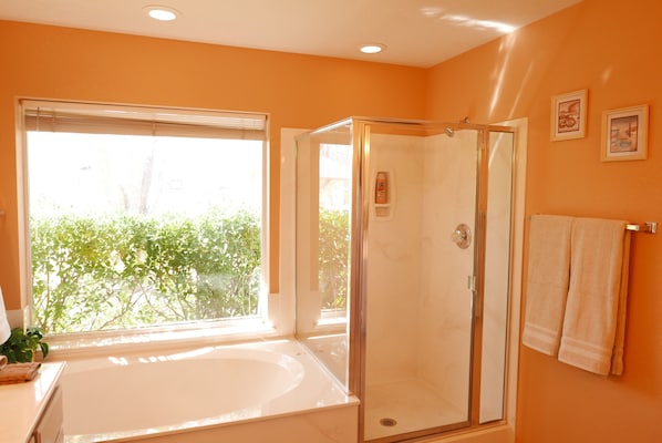 Un baño con ducha envuelta en vidrio, bañera y ventana con persianas.
