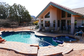 Una casa con piscina, mobiliario de patio y jardín cercado.