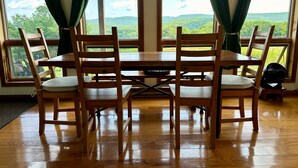 A dining area with a wooden table and chairs, large windows with curtains, and a view of green hills. - Family-Friendly Home With Incredible Berkshire Views And A Private Swim Pond (Stephentown)