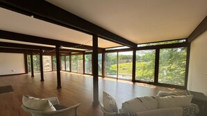 A spacious room with large windows, wooden flooring, and two wicker chairs with cushions. - Family-Friendly Home With Incredible Berkshire Views And A Private Swim Pond (Stephentown)