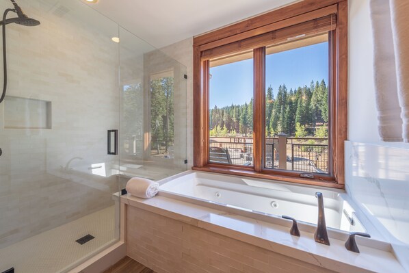 Un baño moderno con ducha envuelta en vidrio, una bañera amplia y un ventanal con vistas a un bosque.
