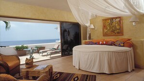 Ein Schlafzimmer mit einem großen Bett, einem Balkon mit Meerblick und tropischer Dekoration.