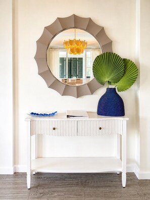 A white console table with a blue vase and a green plant, a round mirror with a geometric frame, and a chandelier. - High Pointe #431 - Gulf Views - 2 min walk to Rosemary (Rosemary Beach)