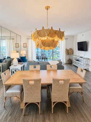 A modern living room with a wooden dining table, wicker chairs, a sofa, and a television.