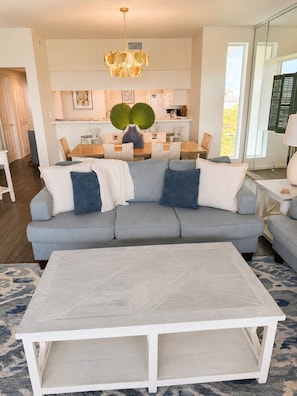 A modern living room with a sectional sofa, a coffee table, and a dining area in the background. - High Pointe #431 - Gulf Views - 2 min walk to Rosemary (Rosemary Beach)