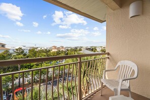 A balcony with a white plastic chair, a metal railing, and a view of a residential area with houses and trees. - High Pointe #431 - Gulf Views - 2 min walk to Rosemary (Rosemary Beach)