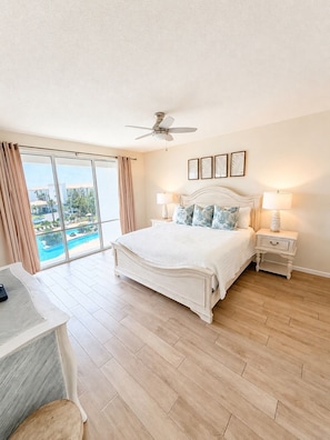 A hotel bedroom with a large bed, two bedside tables with lamps, a ceiling fan, and a view of a swimming pool.