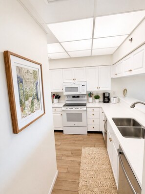 A modern kitchen with white cabinets, a stainless steel sink, and a framed cityscape artwork on the wall.