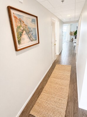 A hallway with a framed painting, a woven rug, and a view into another room. - High Pointe #431 - Gulf Views - 2 min walk to Rosemary (Rosemary Beach)