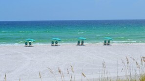 A beach with four green umbrellas and lounge chairs facing the ocean.
