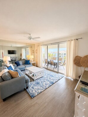 A modern living room with a sofa, coffee table, and a view of the outdoors through large sliding doors. - High Pointe #431 - Gulf Views - 2 min walk to Rosemary (Rosemary Beach)