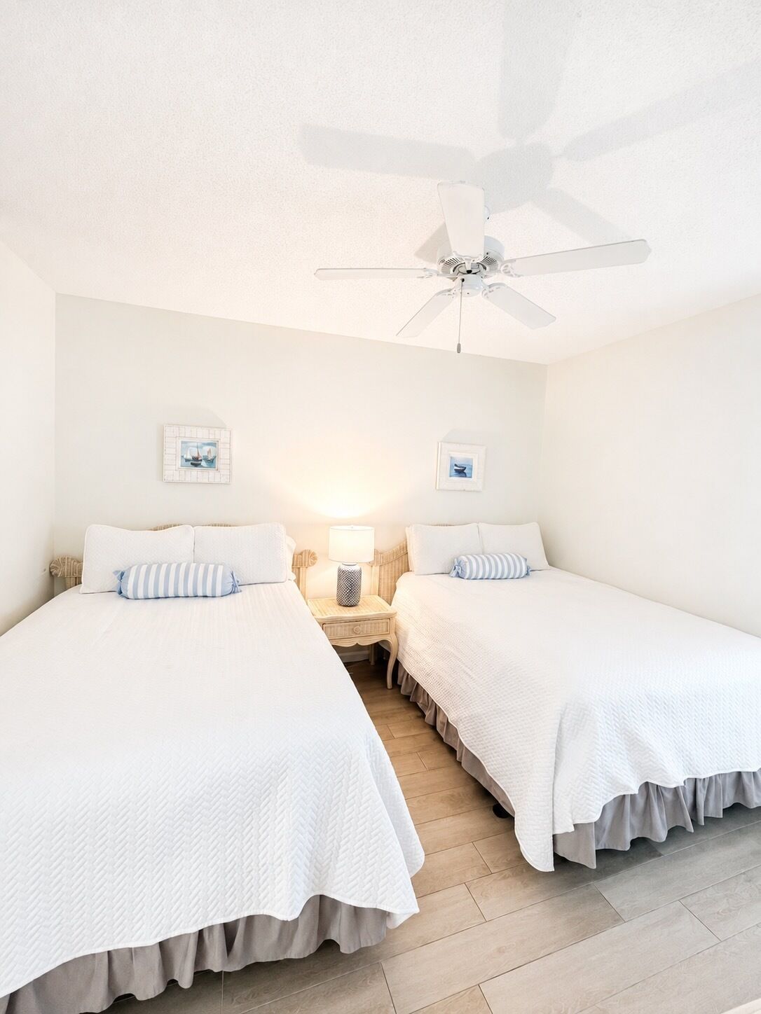 Une chambre d’hôtel avec deux lits, un ventilateur de plafond et une table de chevet avec une lampe.