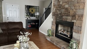 A living room with a stone fireplace, a dark brown leather sofa, a coffee table with decorative items, and a staircase leading to another level. - Charming lakefront home for peaceful mornings and relaxing evenings. (Spring City)