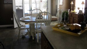 A dining area with a table and chairs, a window with blinds, and a kitchen counter with a tray. - Charming lakefront home for peaceful mornings and relaxing evenings. (Spring City)