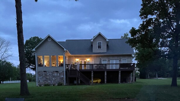 A stone fire pit with logs and flames, surrounded by a stone wall. In the background, there is a house with a stone facade and a deck. - Charming lakefront home for peaceful mornings and relaxing evenings. (Spring City)