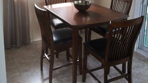 A dining room with a wooden table and chairs, a chandelier, a window with curtains, and a wall clock.