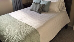 A neatly made bed with a patterned bedspread and pillows, a bedside lamp, and a window with curtains.