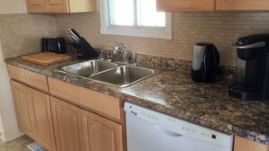 A kitchen with wooden cabinets, a granite countertop, a double sink, a toaster, a coffee maker, and a dishwasher.