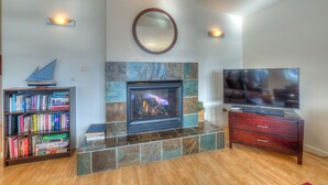 A living room with a fireplace, a television, a bookshelf, and a mirror on the wall. - Water view! 
Luxury Port Suite -- walk to cafes, shops, galleries & beaches. (Eastsound)
