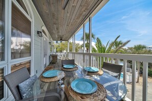 A covered outdoor dining area with wicker chairs and a glass table, surrounded by a white railing. - Gulf views Beach House & Large Private Pool, 2 owner suites; Walk 2 Beach (Panama City Beach)