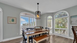 A dining area with a wooden table, chairs, and a bench. There are arched windows and a hanging light fixture. - Gulf views Beach House & Large Private Pool, 2 owner suites; Walk 2 Beach (Panama City Beach)