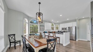 A spacious kitchen with white cabinets, a central island, and a dining area with wooden chairs and a table. - Gulf views Beach House & Large Private Pool, 2 owner suites; Walk 2 Beach (Panama City Beach)