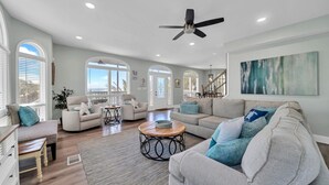 A spacious living room with a ceiling fan, large windows, and a view of the outdoors. - Gulf views Beach House & Large Private Pool, 2 owner suites; Walk 2 Beach (Panama City Beach)