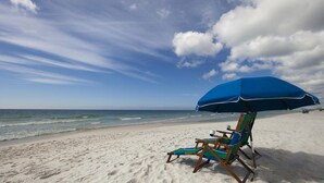 A beach with two wooden beach chairs under a blue umbrella. - Gulf views Beach House & Large Private Pool, 2 owner suites; Walk 2 Beach (Panama City Beach)