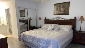 A bedroom with a large bed, wooden headboard, two bedside tables with lamps, a painting on the wall, and a door leading to another room. - A Great Location Five Miles From Major Theme Parks (Kissimmee)