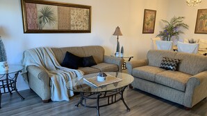 A living room with two sofas, a coffee table, and a lamp. There are framed pictures on the walls and a small table with decorative items. - A Great Location Five Miles From Major Theme Parks (Kissimmee)