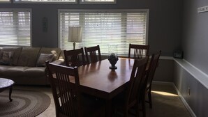 Ein Essbereich mit Holztisch und Stühlen, einer Lampe und Blick auf Bäume durch große Fenster.
