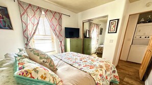 A bedroom with a bed, a television, a wardrobe, and a kitchen area. - Casita D - 2 Bed, 2 Bath (Single Level) (Santa Fe)